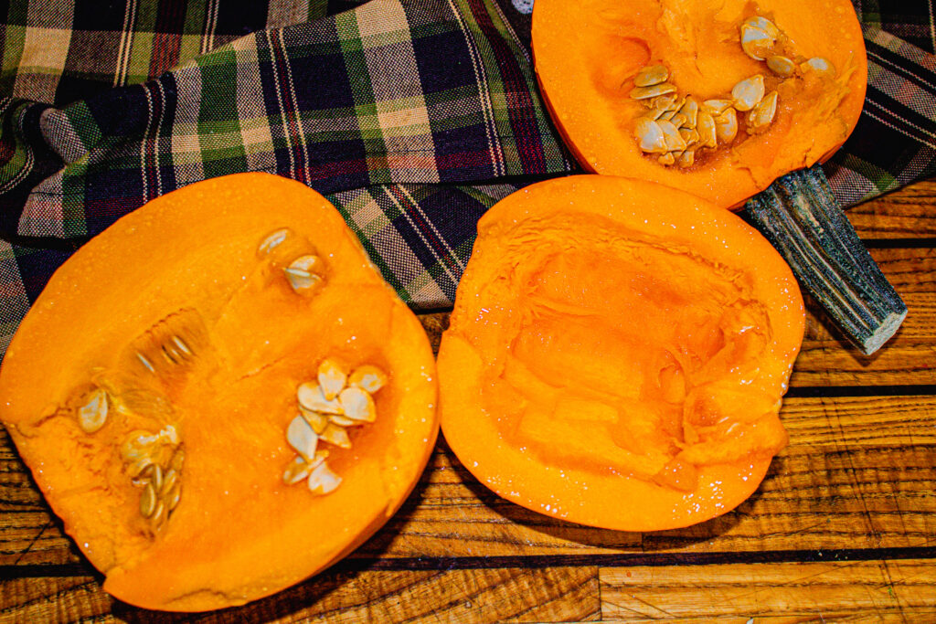 Halved pumpkins on cutting board with seeds carved out ready for sweet & salty pumpkin seeds